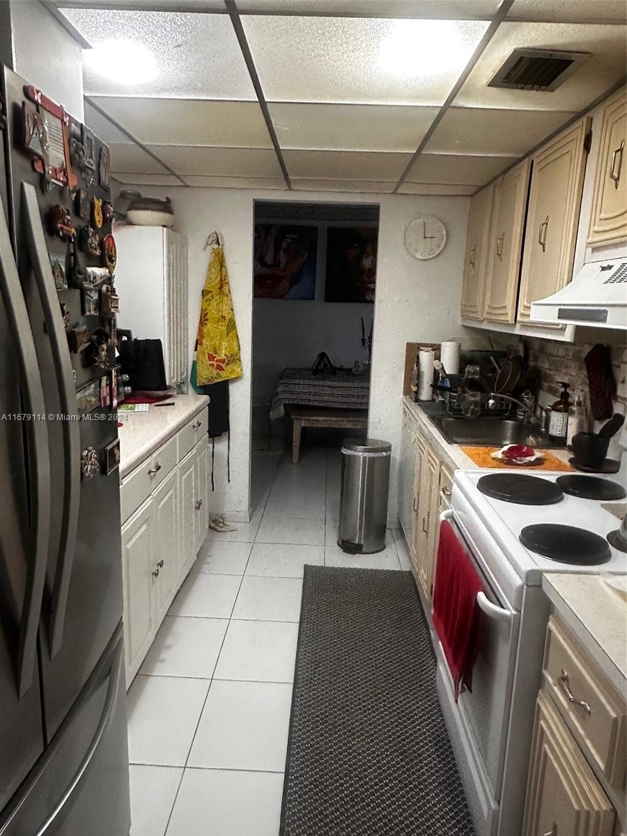 A galley kitchen features white cabinets, a stainless steel refrigerator, and a tiled floor — 3771 Environ Blvd # 151, Lauderhill FL 33319, LAUDERHILL, FL