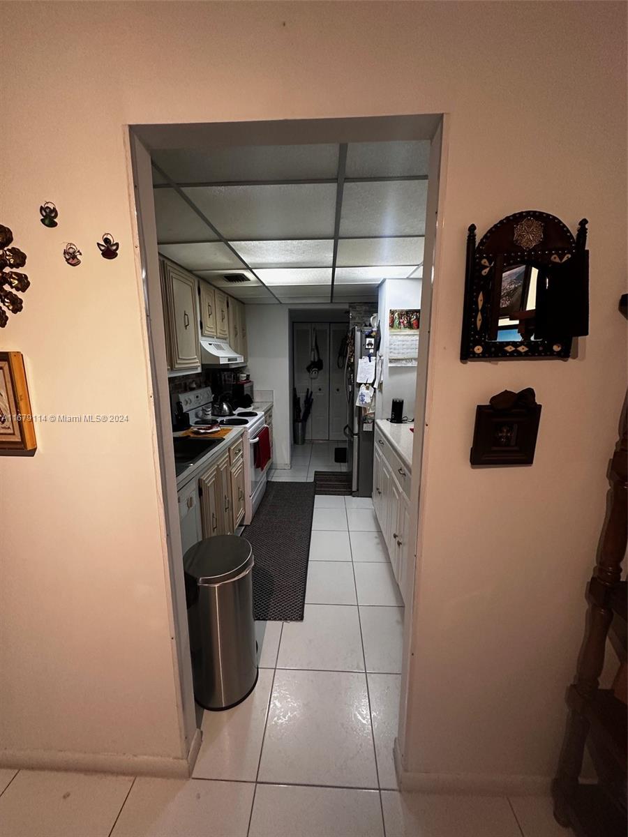 A galley-style kitchen with white cabinets, tiled floors, and a drop ceiling — 3771 Environ Blvd # 151, Lauderhill FL 33319, LAUDERHILL, FL