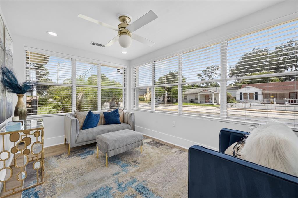 A sunroom features a gray sofa, a blue armchair, and large windows overlooking a street — 413 W PRINCETON STREET, ORLANDO, FL