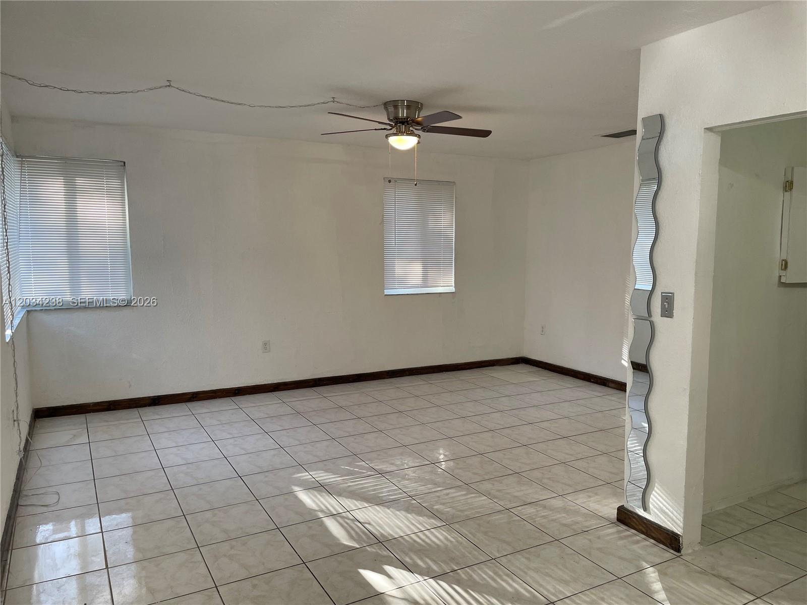 An empty room features white walls, tiled floors, a ceiling fan, and a wavy wall mirror — 3389 William Ave # 0, Miami FL 33133, MIAMI, FL