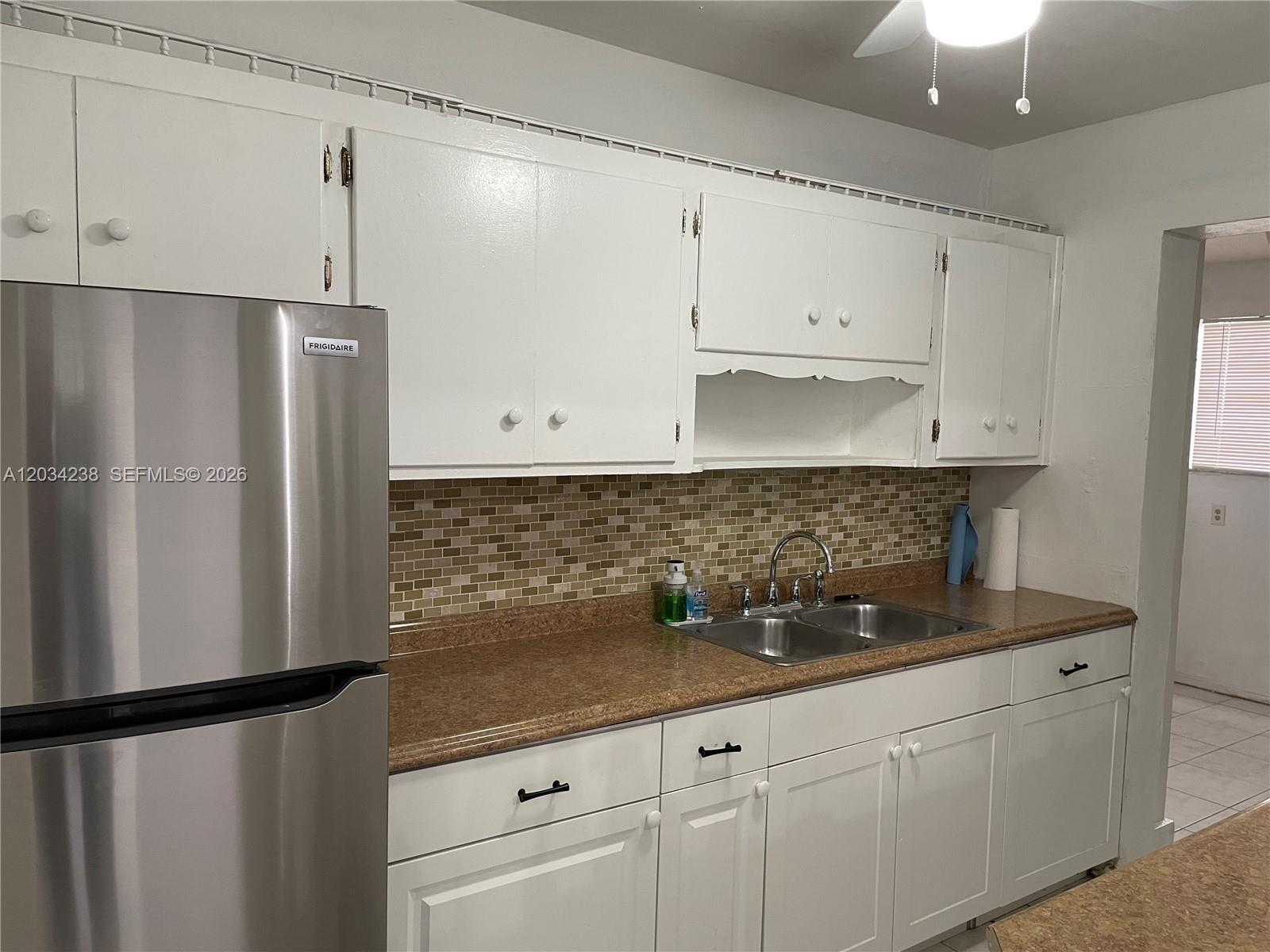 A kitchen features white cabinets, a stainless steel refrigerator, and a brown speckled countertop — 3389 William Ave # 0, Miami FL 33133, MIAMI, FL