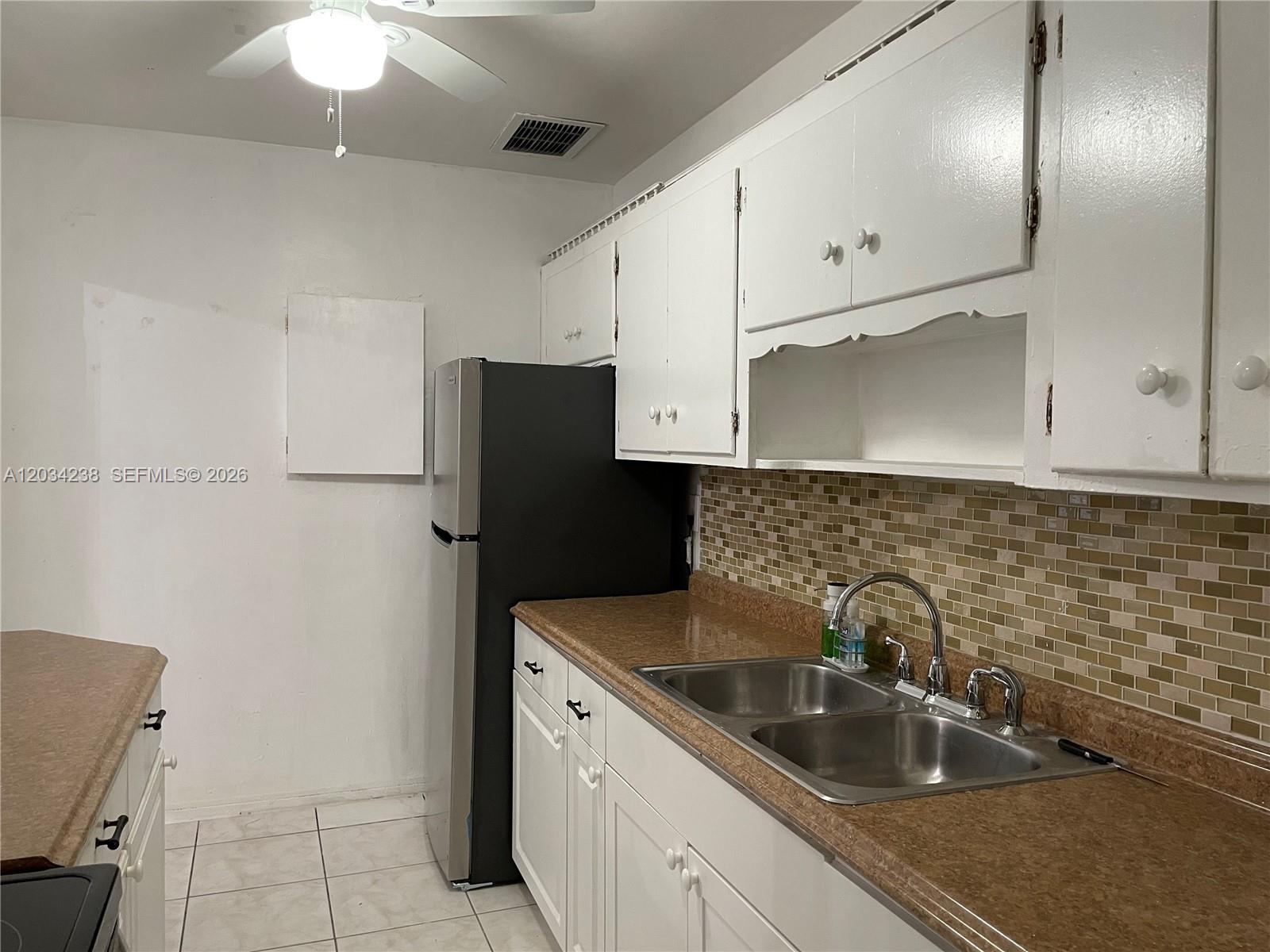 A kitchen features white cabinets, a black refrigerator, a double sink, and a tiled backsplash — 3389 William Ave # 0, Miami FL 33133, MIAMI, FL