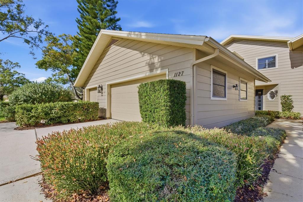 A tan, single-story house exterior features a garage, manicured hedges, and a concrete walkway — 1127 ROYAL TROON COURT, TARPON SPRINGS, FL