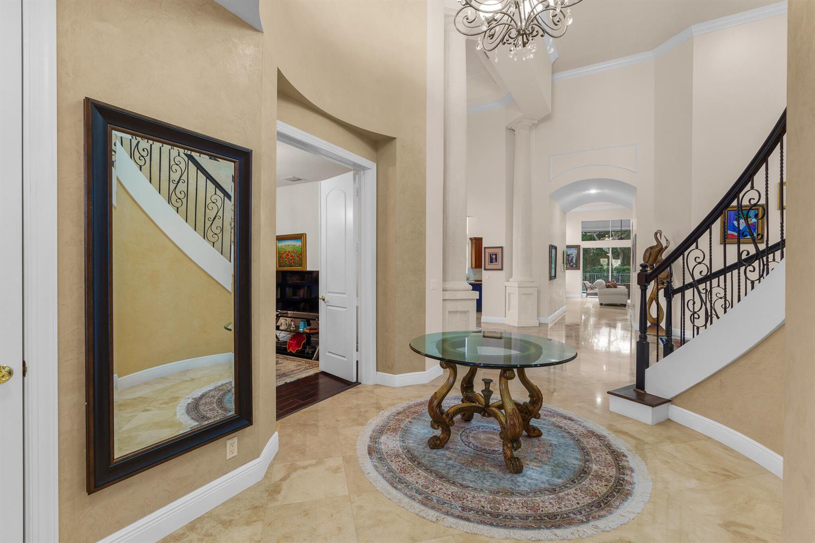 A grand foyer features a glass-topped pedestal table, a circular rug, and a curved staircase — 8850 Valhalla Drive, Delray Beach FL 33446, DELRAY BEACH, FL