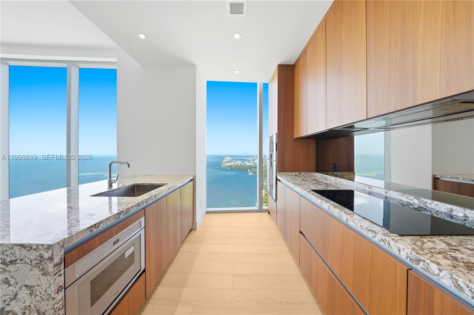 A modern kitchen features wood cabinetry, granite countertops, and floor-to-ceiling windows overlooking the ocean — 175 SE 25th Road # 3102, Miami FL 33129, MIAMI, FL