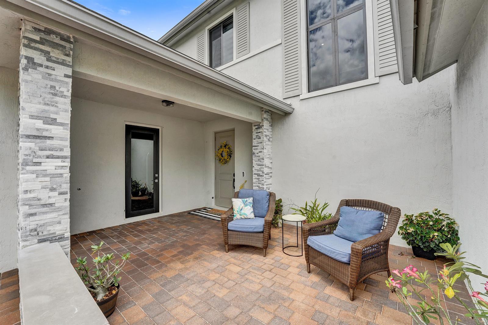A covered entryway features a gray door with a wreath, brick pavers, and a chair — 13025 Addilyn Court, Davie FL 33325, DAVIE, FL