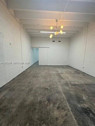 An empty, industrial-style room with white painted brick walls, a concrete floor, and a chandelier — 1825 NW 21st St, Miami FL 33142, MIAMI, FL