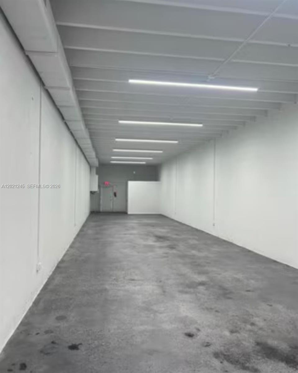 An empty, narrow commercial space features white walls, a concrete floor, and linear ceiling lights — 1825 NW 21st St, Miami FL 33142, MIAMI, FL