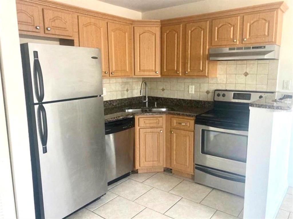 A kitchen features light wood cabinets, stainless steel appliances, dark countertops, and tiled flooring — 4772 WALDEN CIRCLE UNIT 11, ORLANDO, FL