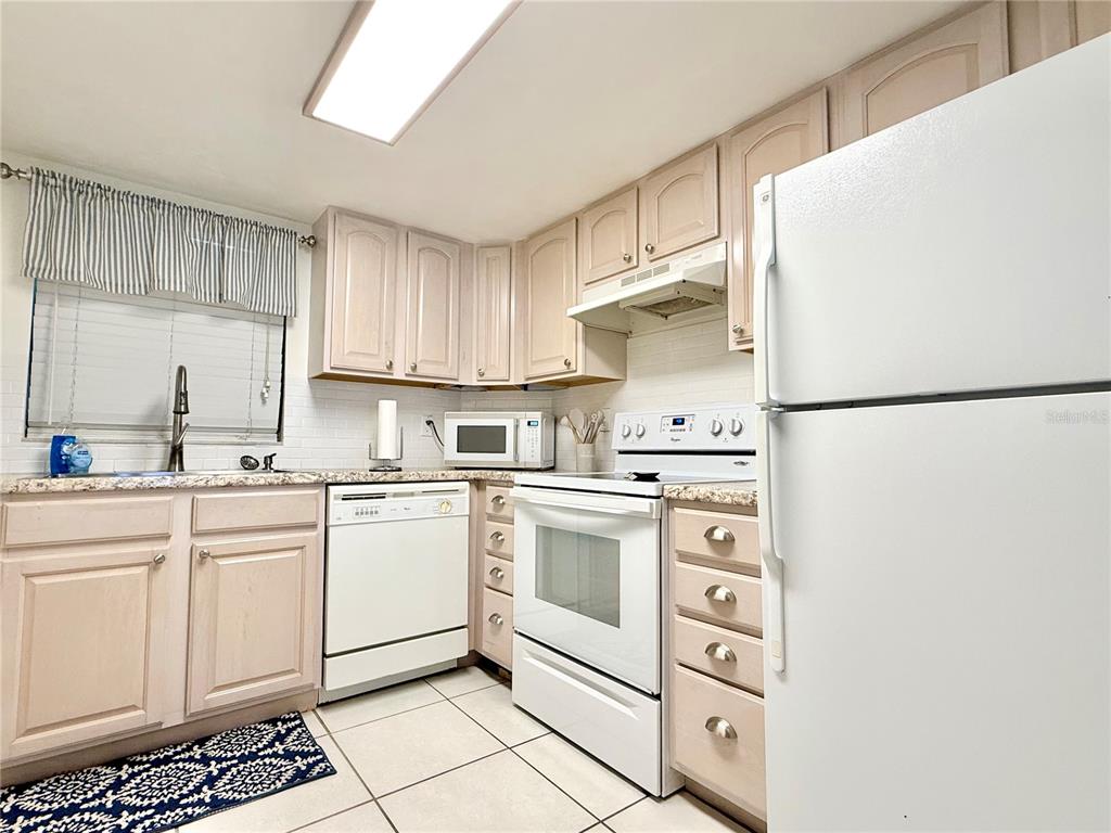A kitchen features light-colored cabinets, white appliances, a tiled backsplash, and granite countertops — 3800 S ATLANTIC AVENUE UNIT 105, DAYTONA BEACH, FL