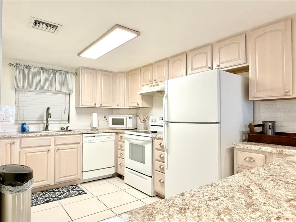 A kitchen features white appliances, light-colored cabinets, tiled flooring, and a breakfast bar — 3800 S ATLANTIC AVENUE UNIT 105, DAYTONA BEACH, FL