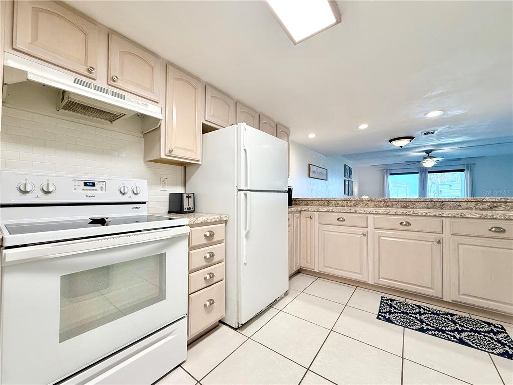 A kitchen with granite countertops overlooks a living room with a sofa and ceiling fan — 3800 S ATLANTIC AVENUE UNIT 105, DAYTONA BEACH, FL