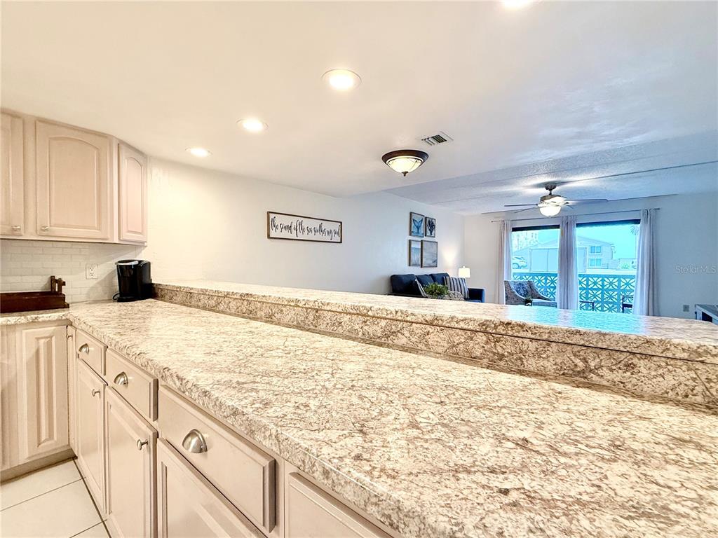 A dining area with a wooden table and metal chairs sits before a kitchen breakfast bar — 3800 S ATLANTIC AVENUE UNIT 105, DAYTONA BEACH, FL