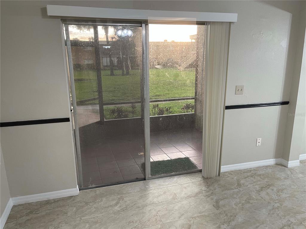 A room with tile flooring features a sliding glass door leading to a covered patio — 1000 LAKE OF THE WOODS BOULEVARD UNIT F106, FERN PARK, FL