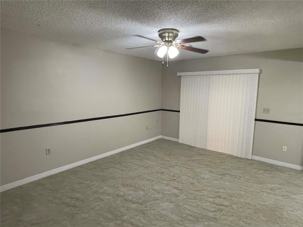An empty room features light-colored walls with a dark chair rail, tile flooring, and a ceiling fan — 1000 LAKE OF THE WOODS BOULEVARD UNIT F106, FERN PARK, FL