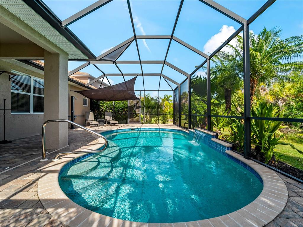 A screened-in swimming pool with a water feature sits on a paved patio — 11631 DANCING RIVER DR, VENICE, FL