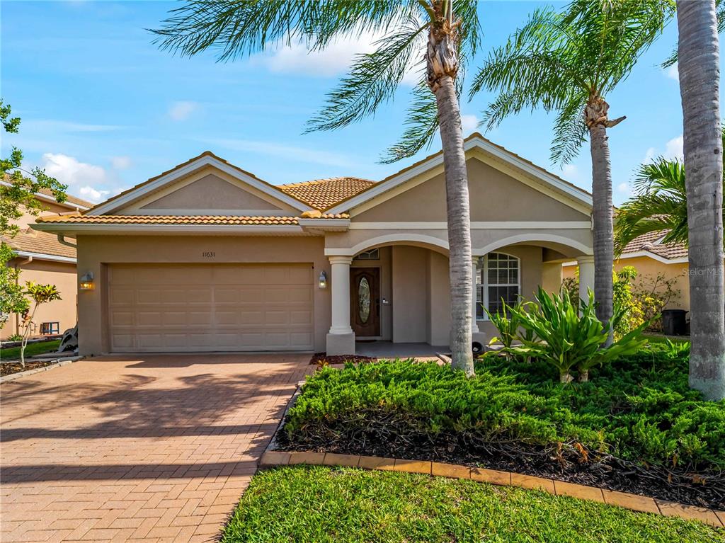A single-story house with a tan stucco exterior, a paved driveway, and palm trees — 11631 DANCING RIVER DR, VENICE, FL