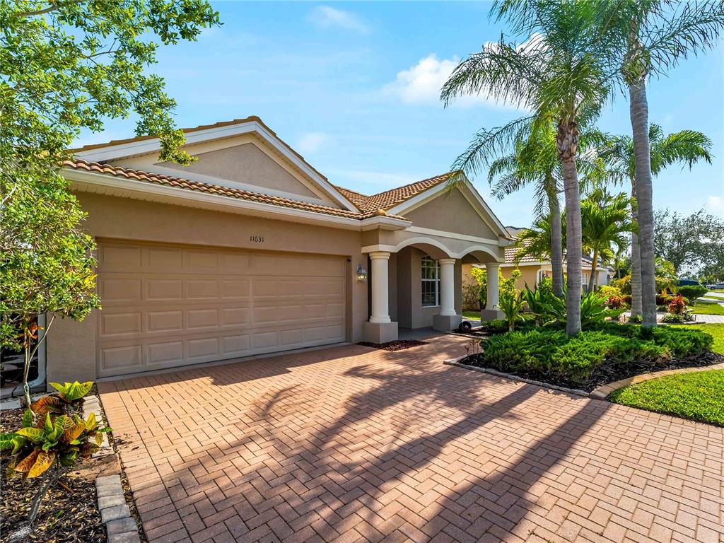 The exterior of a single-story house features a tan stucco facade, a brick-paved driveway, and palm trees — 11631 DANCING RIVER DR, VENICE, FL