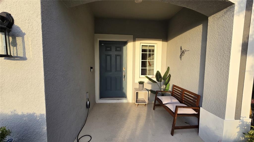 A covered front porch features a blue door, a wooden bench, and a wall-mounted charger — 3609 ANIBAL STREET, KISSIMMEE, FL