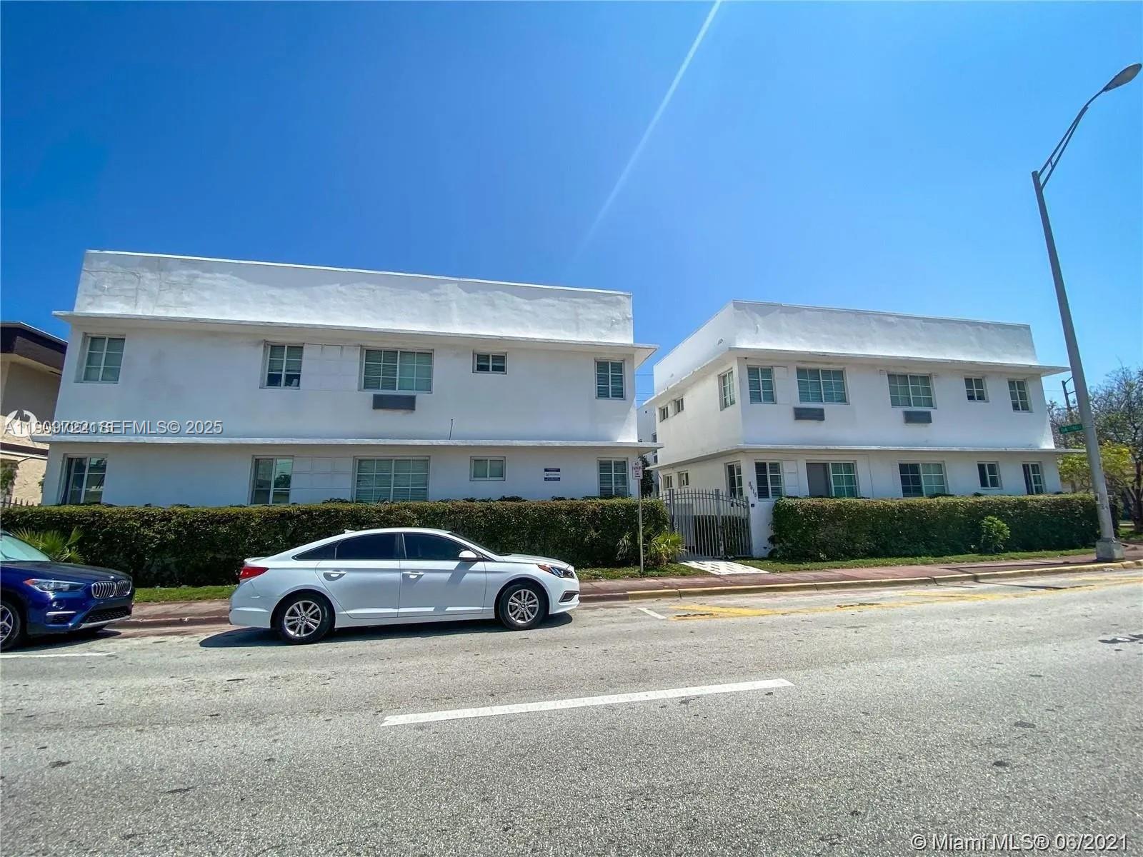 Two white two-story apartment buildings stand behind a hedge with a car parked in front — 8415 Harding Ave # 5, Miami Beach FL 33141, MIAMI BEACH, FL