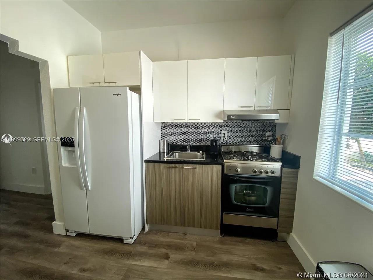 A kitchen features white upper cabinets, wood-grain lower cabinets, a gas range, and a refrigerator — 8415 Harding Ave # 5, Miami Beach FL 33141, MIAMI BEACH, FL