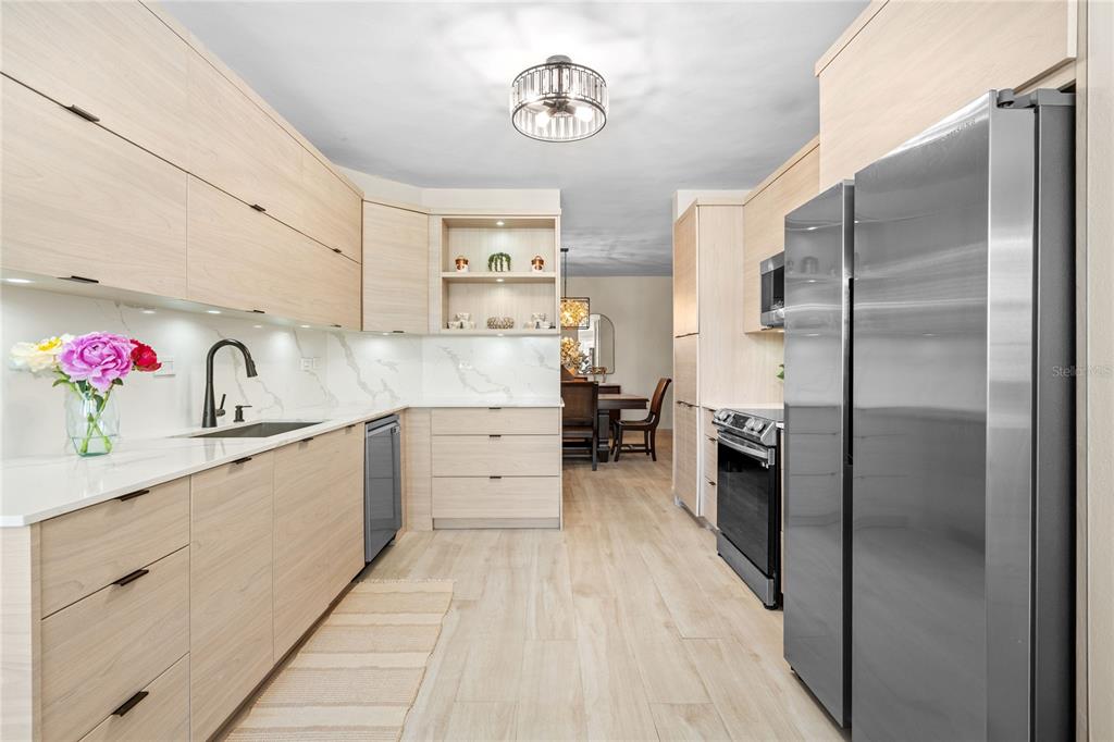 A modern kitchen features light wood cabinetry, stainless steel appliances, and white marble-patterned countertops — 6690 Rd. ROYAL PALM COND. UNIT D-101, VEGA ALTA, PR