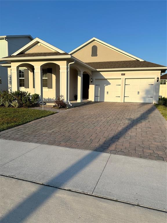 A single-story house with a beige stucco exterior, a paver driveway, and a two-car garage — 14827 MILFOIL AVENUE, ORLANDO, FL
