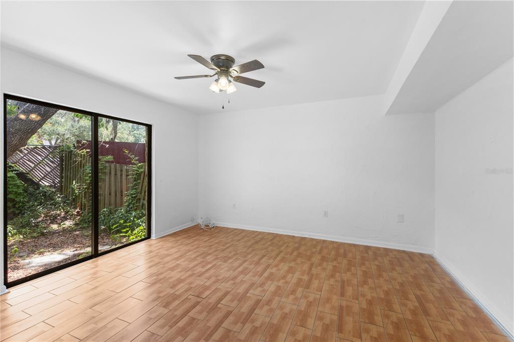 An empty room features wood-look tile flooring, white walls, a ceiling fan, and sliding doors — 5641 ASHLEY OAKS DRIVE UNIT 37, TAMPA, FL