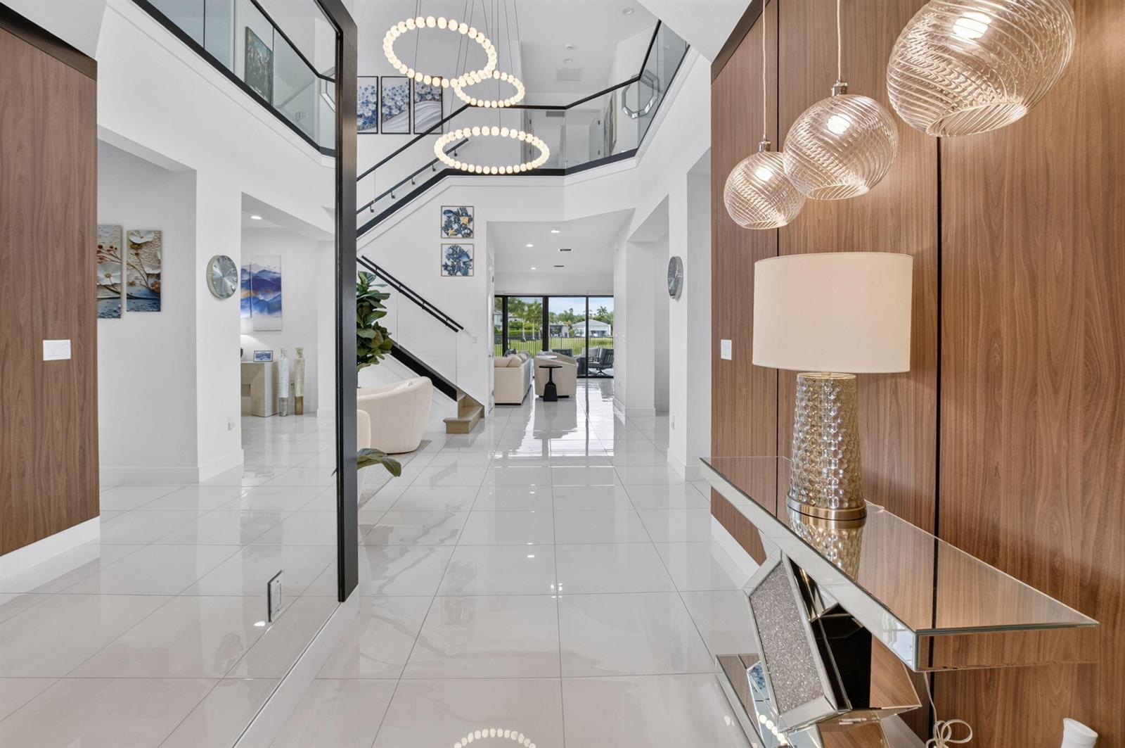 A modern, two-story foyer features white tile floors, a glass-railed staircase, and decorative pendant lighting — 20056 Hirono Lane, Boca Raton FL 33434, BOCA RATON, FL