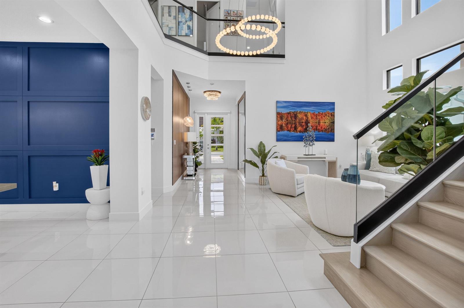 A bright, modern foyer features white tile floors, a blue accent wall, and a staircase — 20056 Hirono Lane, Boca Raton FL 33434, BOCA RATON, FL