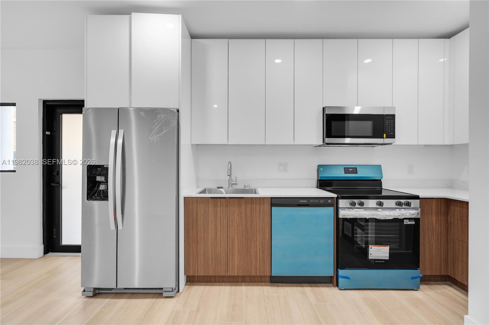 A modern kitchen features white upper cabinets, wood-tone lower cabinets, and stainless steel appliances — 1037 NW 2nd St # 3C, Miami FL 33128, MIAMI, FL