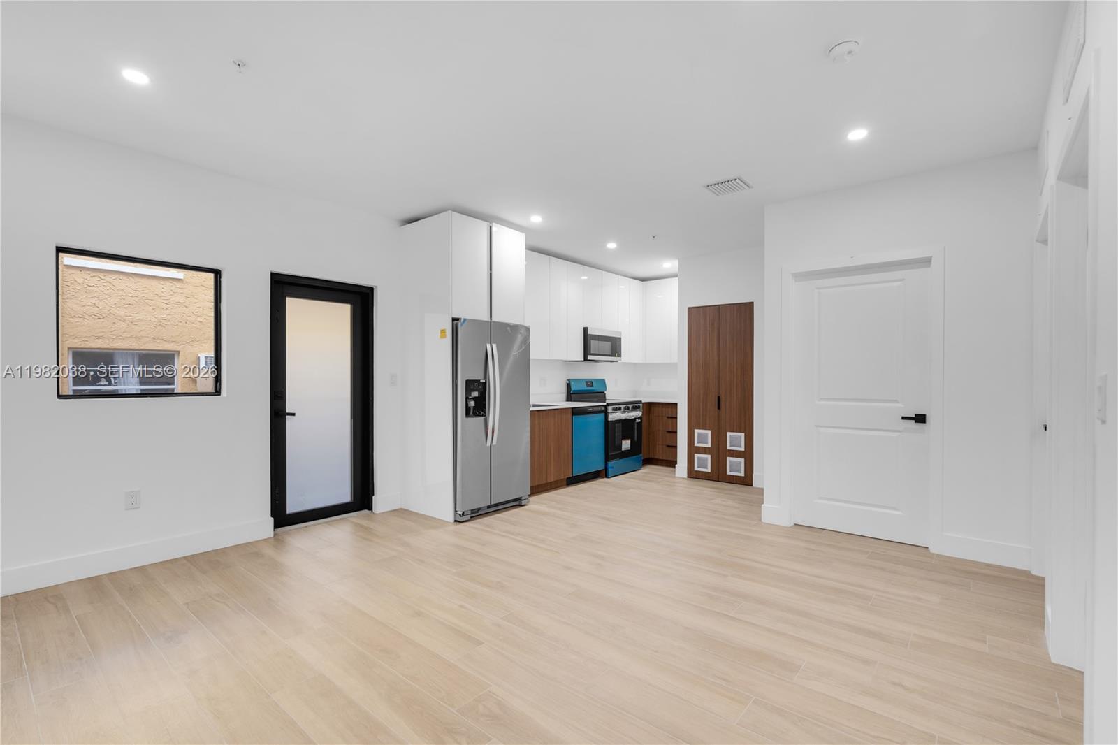 A modern kitchen features white upper cabinets, wood-toned lower cabinets, and light wood flooring — 1037 NW 2nd St # 3C, Miami FL 33128, MIAMI, FL