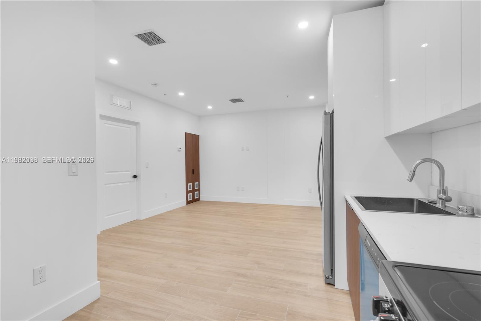 This kitchen and living area features white cabinetry, light wood-look flooring, and recessed lighting — 1037 NW 2nd St # 3C, Miami FL 33128, MIAMI, FL