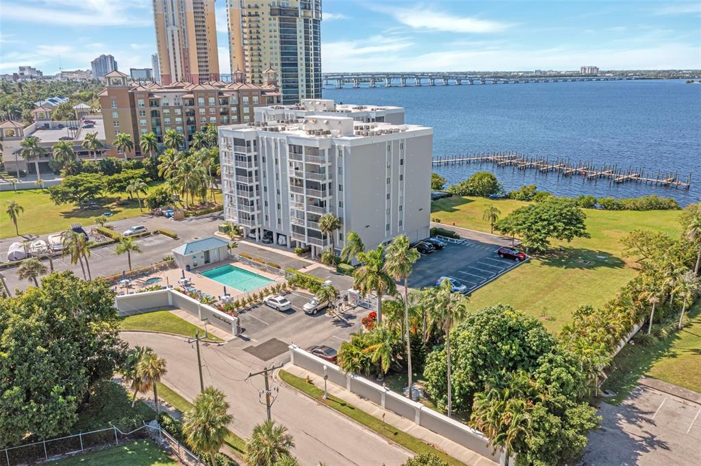 An aerial view shows a multi-story apartment building with a pool and waterfront access — 2875 PALM BEACH BOULEVARD UNIT 205, FORT MYERS, FL
