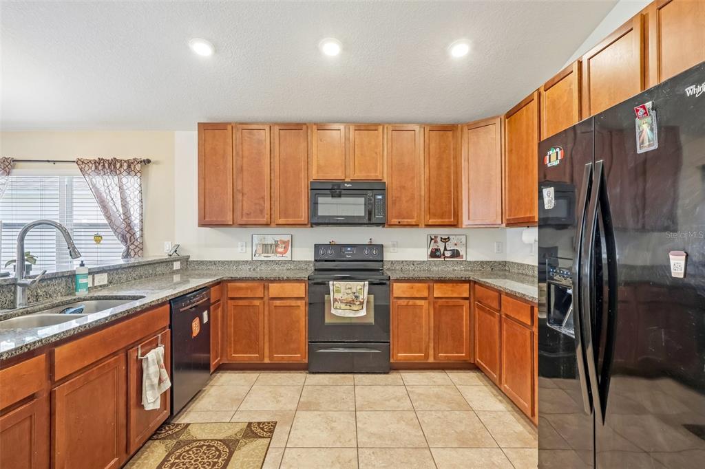 A kitchen features wood cabinets, granite countertops, black appliances, and tile flooring — 14284 FINSBURY DRIVE, SPRING HILL, FL