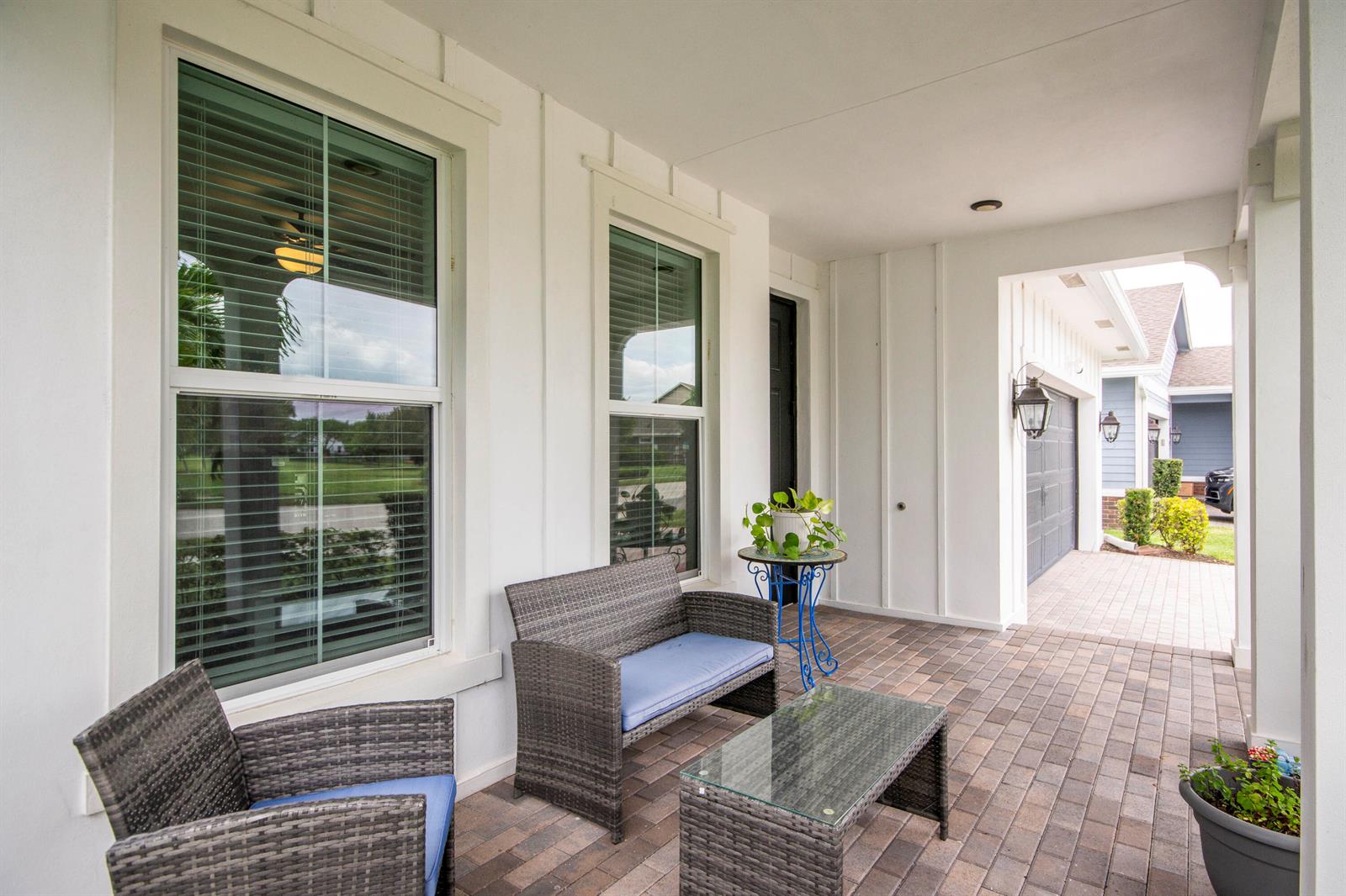 A covered porch features brick pavers, wicker furniture, and white board-and-batten siding — 889 Wandering Willow Way, Loxahatchee FL 33470, LOXAHATCHEE, FL