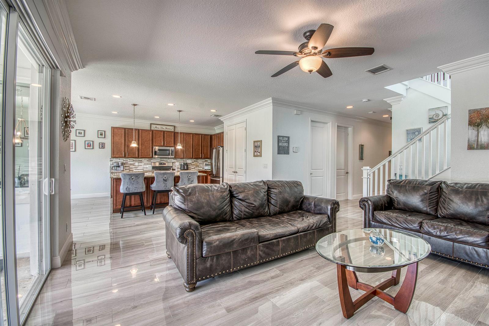 A living room with dark leather sofas and a glass coffee table faces an open kitchen — 889 Wandering Willow Way, Loxahatchee FL 33470, LOXAHATCHEE, FL
