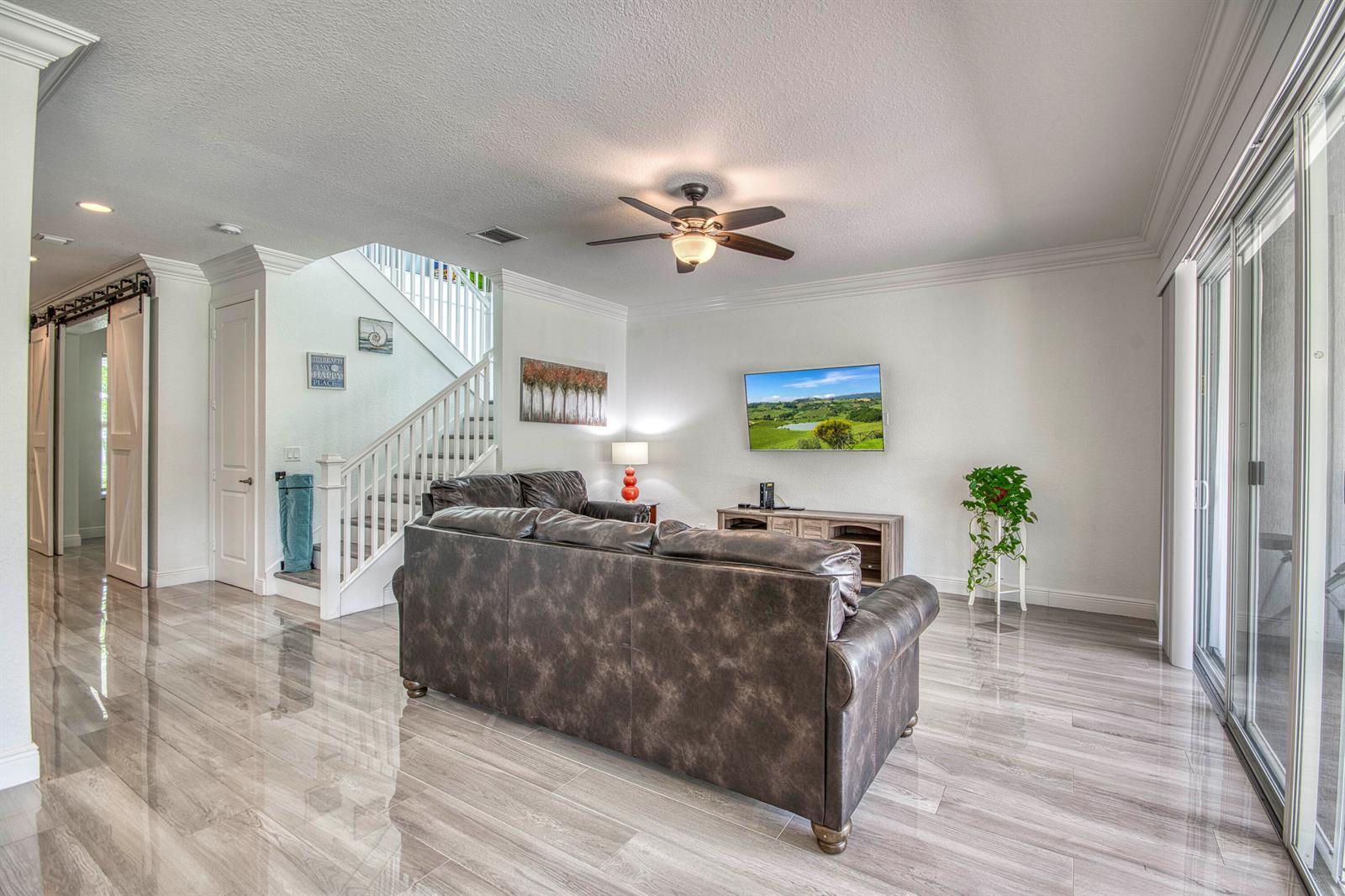 A living room features a dark leather sofa, wood-look tile flooring, and a staircase — 889 Wandering Willow Way, Loxahatchee FL 33470, LOXAHATCHEE, FL