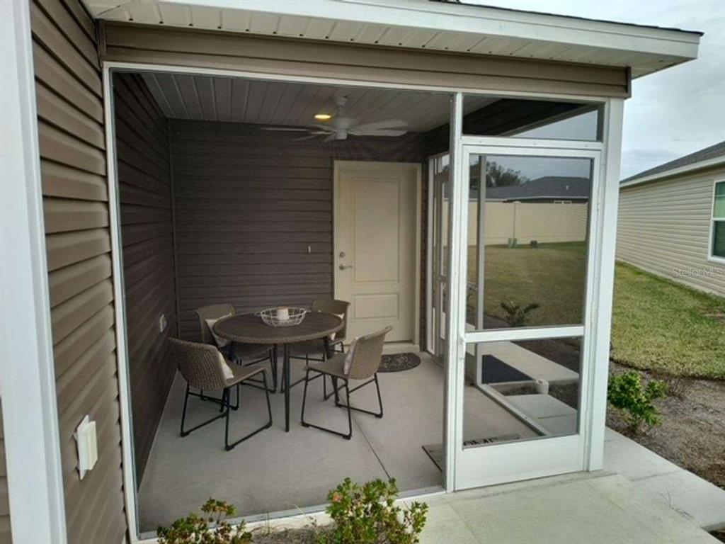 A screened-in patio with a dining set, ceiling fan, and a door leading indoors — 2845 CHARITY LOOP, THE VILLAGES, FL