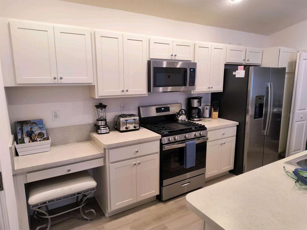A kitchen features white cabinets, stainless steel appliances, and a small built-in desk area — 2845 CHARITY LOOP, THE VILLAGES, FL