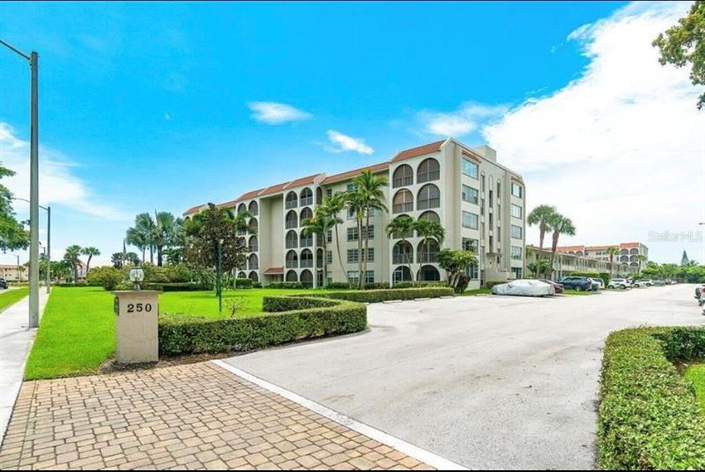 A multi-story apartment building with balconies stands behind a parking lot and manicured lawn — 250 NE 20TH STREET UNIT 3030, BOCA RATON, FL