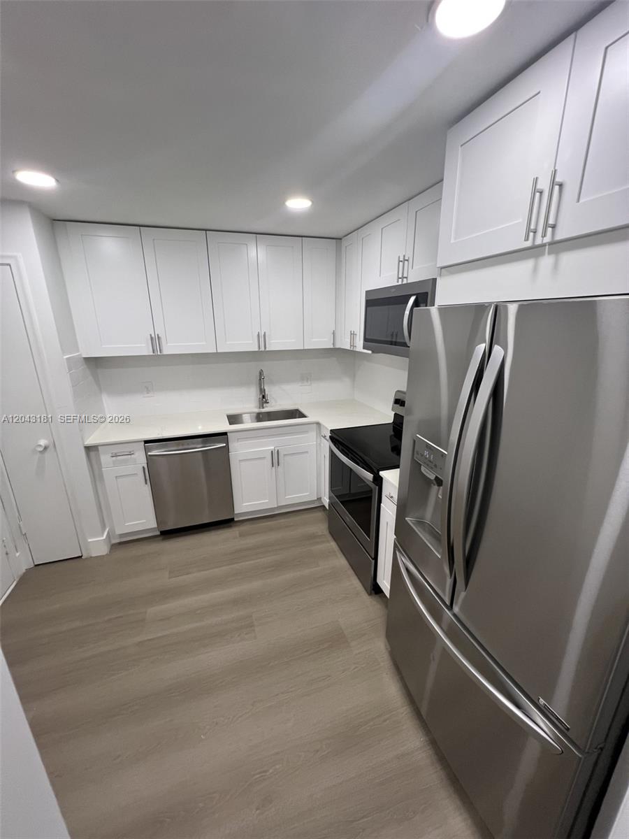 A modern kitchen features white cabinets, stainless steel appliances, and light wood-look flooring — 22605 SW 66th Ave # 403, Boca Raton FL 33428, BOCA RATON, FL
