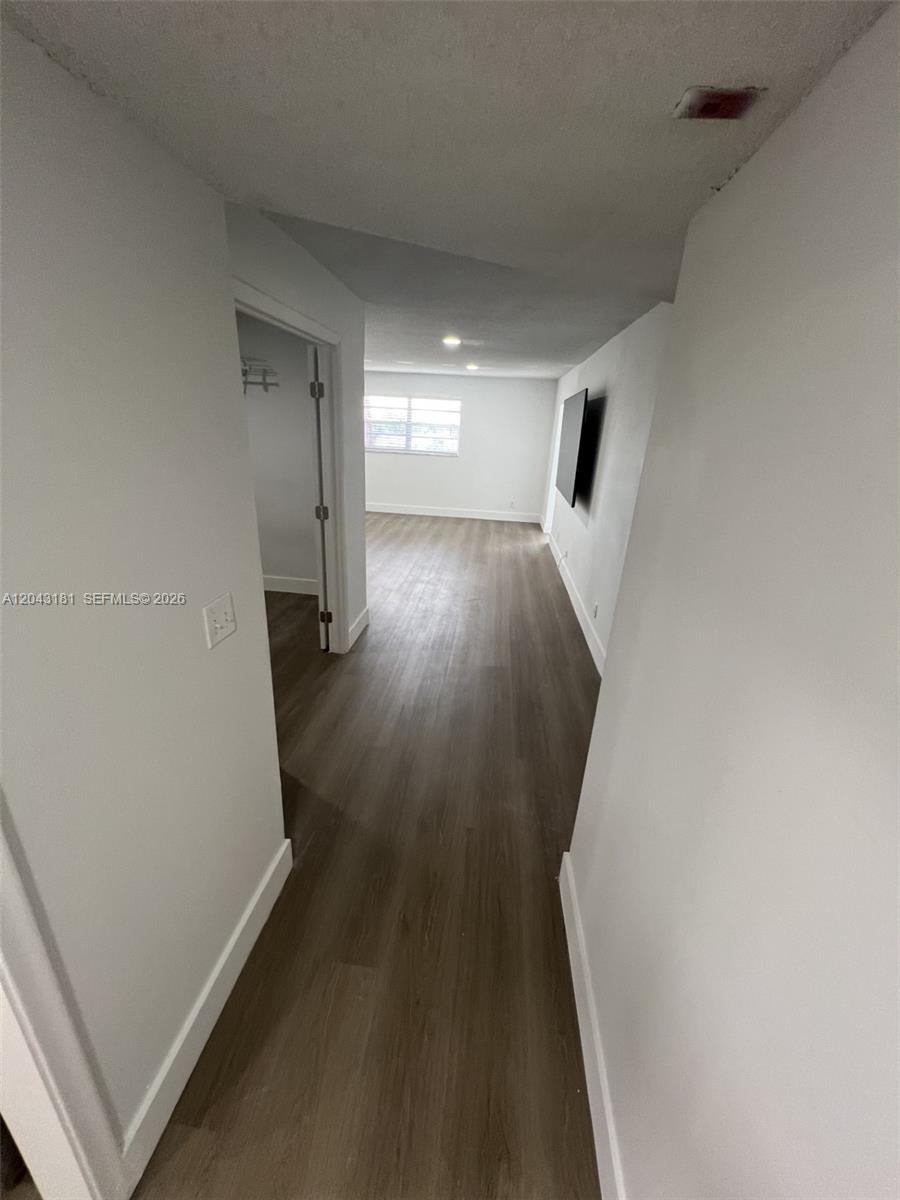 A hallway with wood-look flooring leads into a living area with a wall-mounted television — 22605 SW 66th Ave # 403, Boca Raton FL 33428, BOCA RATON, FL