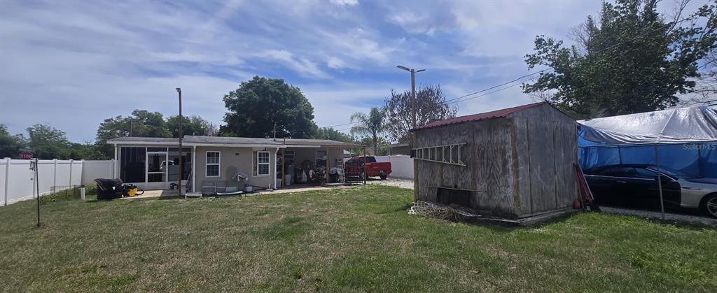 A backyard features a house with a screened porch, a wooden shed, and a car shelter — 1222 STILLWATER AVENUE, DELTONA, FL