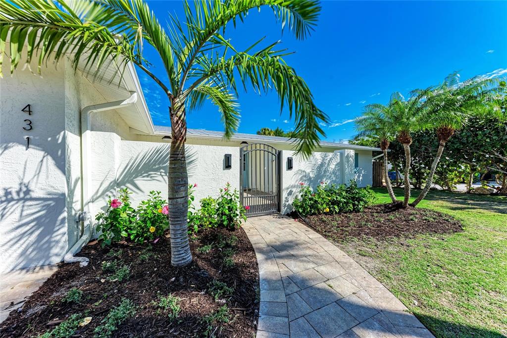 A paved walkway leads to a gated entrance of a white house with palm trees — 431 ISLAND CIRCLE, SARASOTA, FL