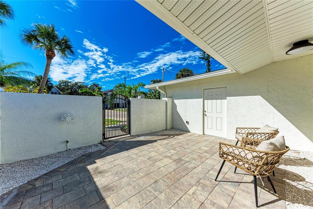 A paved patio features two wicker chairs, a white privacy wall, and a metal gate — 431 ISLAND CIRCLE, SARASOTA, FL