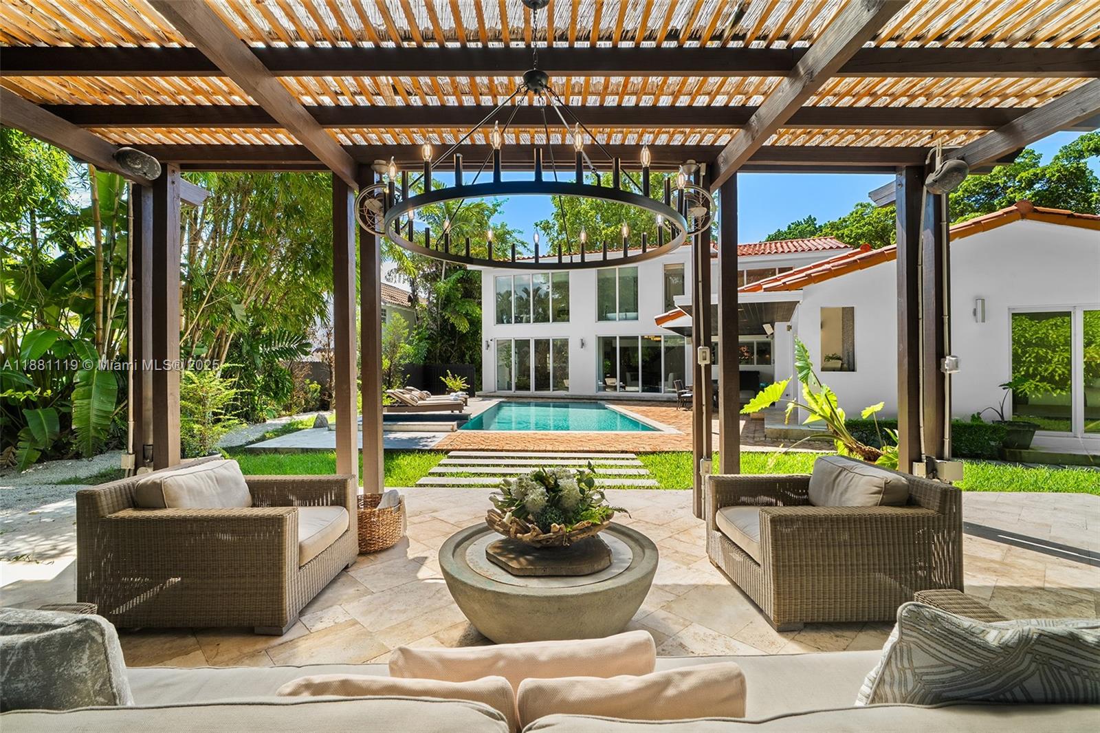 A covered patio features wicker seating, a stone coffee table, and a view of a pool — 575 Bay Point Rd, Miami FL 33137, MIAMI, FL