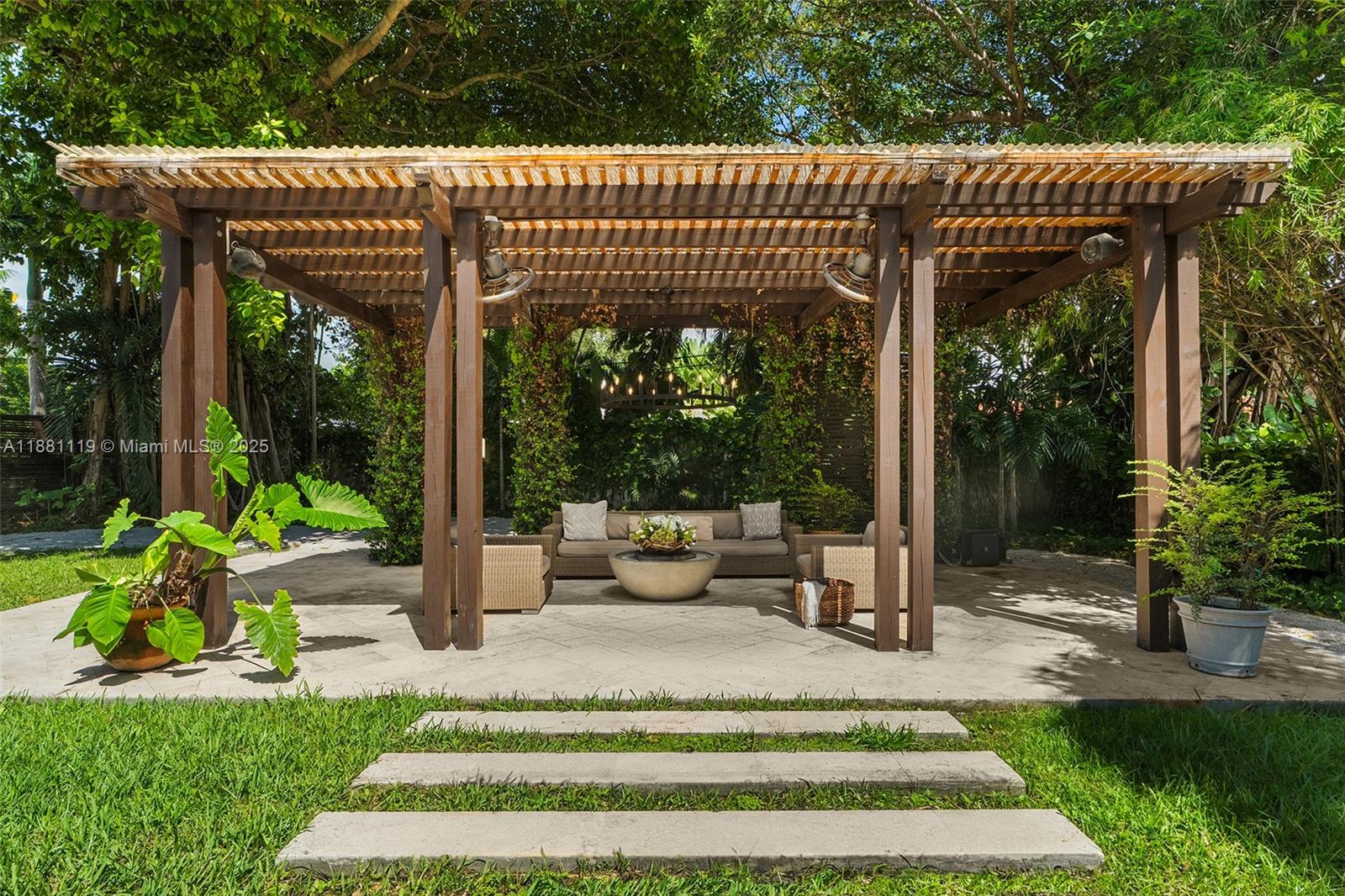 A wooden pergola covers a patio with outdoor seating, a fire pit, and lush landscaping — 575 Bay Point Rd, Miami FL 33137, MIAMI, FL