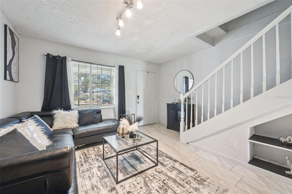 A living room features a black sectional sofa, a glass coffee table, and a staircase — 6924 WOODLAKE UNIT 104, ORLANDO, FL