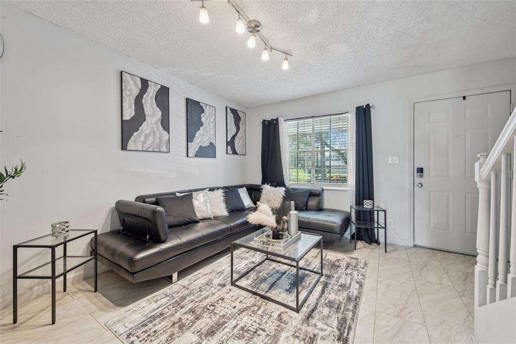 A living room features a black sectional sofa, glass tables, and a patterned area rug — 6924 WOODLAKE UNIT 104, ORLANDO, FL